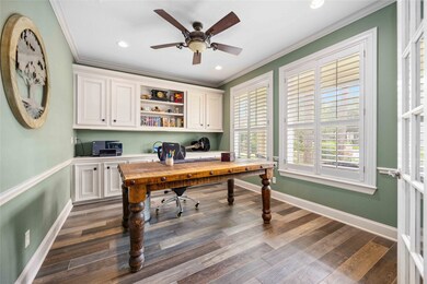 Home office with white cabinetry, patterned floors, green walls, and a ceiling fan. Natural light streams in through shuttered windows.