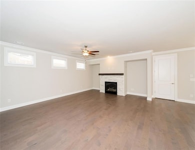 Unfurnished living room with ornamental molding, dark wood-style flooring, a fireplace, and a ceiling fan