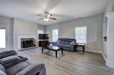 Living area featuring ceiling fan, light wood-style flooring, baseboards, and a stone fireplace
