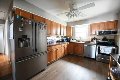 Kitchen featuring appliances with stainless steel finishes, wood finished floors, a ceiling fan, dark countertops, and brown cabinets