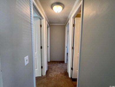 Hallway featuring dark colored carpet, a textured 