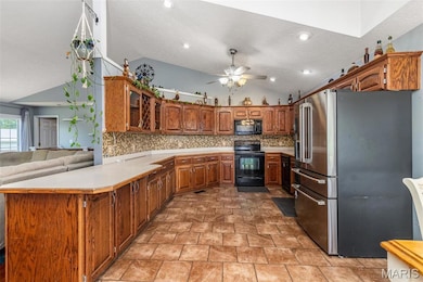 Kitchen with black appliances, lofted ceiling, brown cabinetry, backsplash, and a peninsula