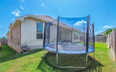 Rear view of house featuring a trampoline, a fenced backyard, and brick siding