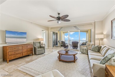 Living room featuring crown molding, a ceiling fan, stone tile floors, beach views