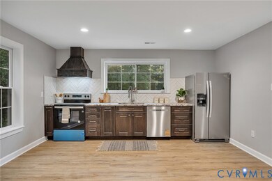 Kitchen featuring dark brown cabinets, stainless steel appliances, light wood-style floors, backsplash, and custom exhaust hood