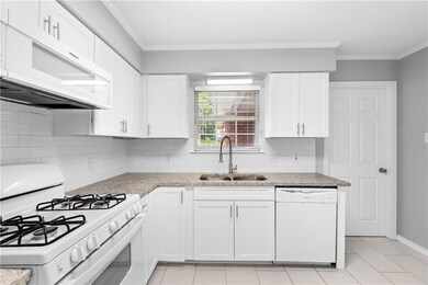 Kitchen featuring white appliances, a sink, crown molding, white cabinets, and decorative backsplash