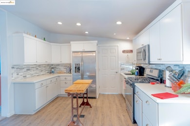 Kitchen featuring stainless steel appliances, light wood finished floors, lofted ceiling, backsplash, and white cabinetry