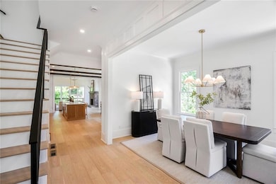 Entrance foyer with large dining room, featuring board and batten walls, crown molding, an inviting chandelier, striking, custom black handrailsl and a healthy amount of sunlight.