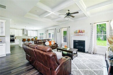Living area with dark wood-style flooring, beam ceiling, a ceiling fan, a fireplace with flush hearth, and coffered ceiling
