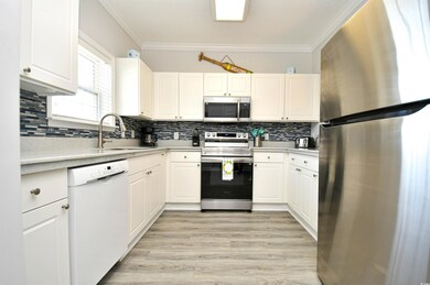 Kitchen with appliances with stainless steel finishes, ornamental molding, light countertops, backsplash, and white cabinets