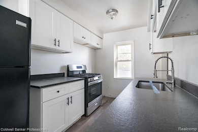 Kitchen featuring dark countertops, freestanding refrigerator, gas stove, and white cabinetry