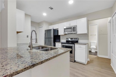 Kitchen with stainless steel appliances, white cabinets, tasteful backsplash, light stone counters, and light wood-style floors