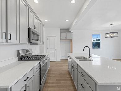 Kitchen with gray cabinets, appliances with stainless steel finishes, a center island with sink, light wood-style flooring, and recessed lighting