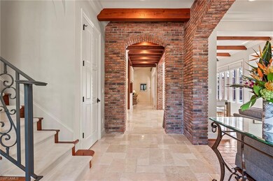 Hallway with travertine tile floors, beam ceiling, stairs to guest wing, arched walkways, brick accents