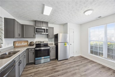 Kitchen featuring sink, a textured ceiling, light hardwood / wood-style floors, gray cabinets, and appliances with stainless steel finishes
