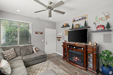 Living area featuring wood finished floors, recessed lighting, a glass covered fireplace, and a ceiling fan