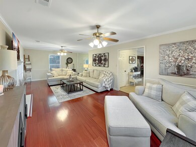 Living room with crown molding, dark wood-type flooring, and a ceiling fan