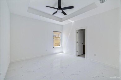 Empty room featuring a tray ceiling, a ceiling fan, and light marble finish floors