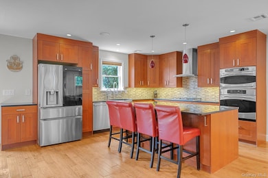 Kitchen with appliances with stainless steel finishes, brown cabinetry, a breakfast bar area, dark stone counters, and recessed lighting