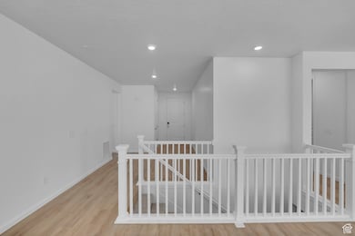 Hallway featuring an upstairs landing, light wood-style floors, and recessed lighting