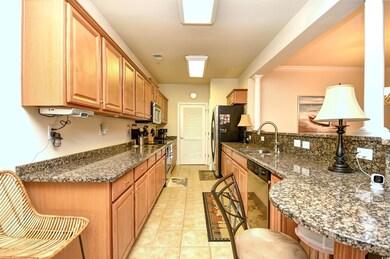 Kitchen featuring appliances with stainless steel finishes, a peninsula, a kitchen bar, dark stone countertops, and light tile patterned floors