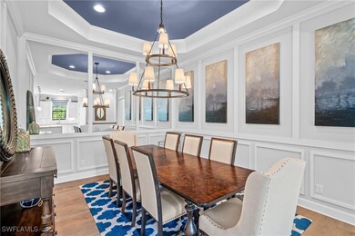 Dining area with a tray ceiling, a decorative wall, crown molding, light wood-style floors, and a chandelier