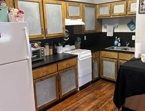 Kitchen featuring white appliances, dark countertops, brown cabinets, dark wood-style flooring, and range hood