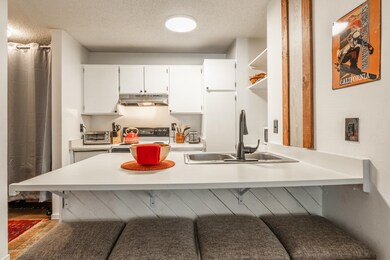 Kitchen with light countertops, white cabinetry, open shelves, a kitchen breakfast bar, and a textured ceiling