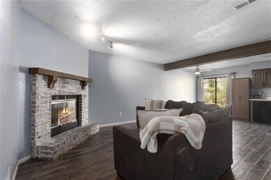 Living room featuring a fireplace, a textured ceiling, beam ceiling, dark hardwood / wood-style flooring, and ceiling fan