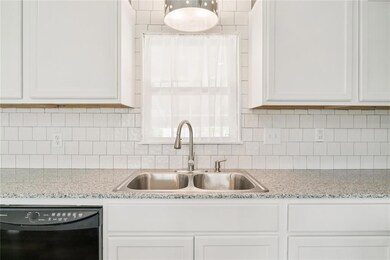 Kitchen with black dishwasher, a sink, white cabinets, tasteful backsplash, and light stone countertops