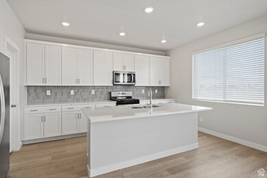 Kitchen featuring light countertops, stainless steel appliances, decorative backsplash, and a sink