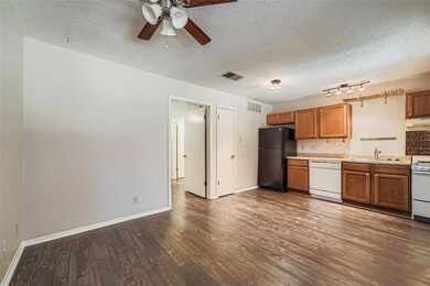 Kitchen with a textured ceiling, brown cabinets, white appliances, wood finished floors, and light countertops