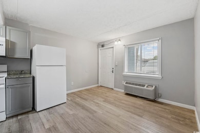 Kitchen with white appliances, light wood-style flooring, a textured ceiling, gray cabinetry, and a wall mounted AC