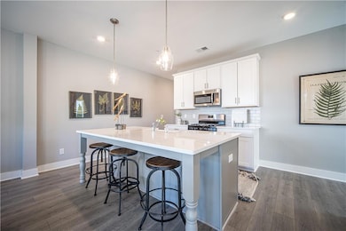 Kitchen with appliances with stainless steel finishes, baseboards, dark wood-style flooring, a center island with sink, and recessed lighting