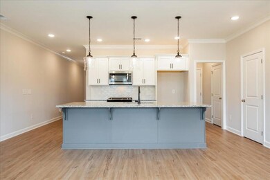 MODEL REPRESENTATIVE- Kitchen with white cabinetry, decorative light fixtures, backsplash, stainless steel microwave, and crown molding