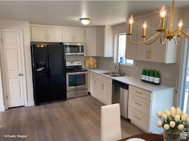 Kitchen featuring appliances with stainless steel finishes, white cabinets, pendant lighting, dark wood-type flooring, and light stone counters