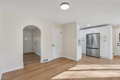 Kitchen featuring white cabinetry, arched walkways, freestanding refrigerator, light wood-type flooring, and light countertops