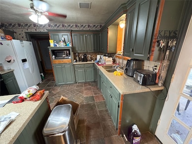 Kitchen with white refrigerator with ice dispenser, light countertops, green cabinetry, dark stone finish flooring, and a ceiling fan