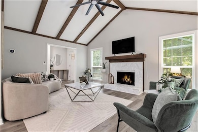 Living room featuring high vaulted ceiling, a ceiling fan, a premium fireplace, beam ceiling, and wood finished floors