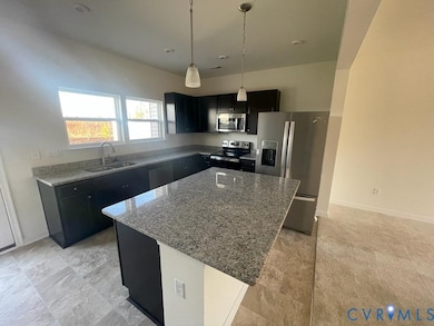Kitchen with dark cabinets, appliances with stainless steel finishes, light stone counters, decorative light fixtures, and a kitchen island
