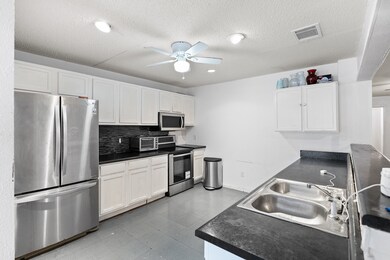 Kitchen featuring stainless steel appliances, dark countertops, white cabinetry, decorative backsplash, and a ceiling fan