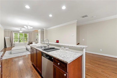 Kitchen with stainless steel dishwasher, crown molding, light wood-type flooring, open floor plan, and a center island with sink