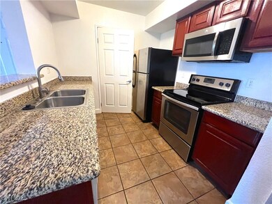 Kitchen featuring appliances with stainless steel finishes, light tile patterned flooring, light stone countertops, and dark brown cabinets
