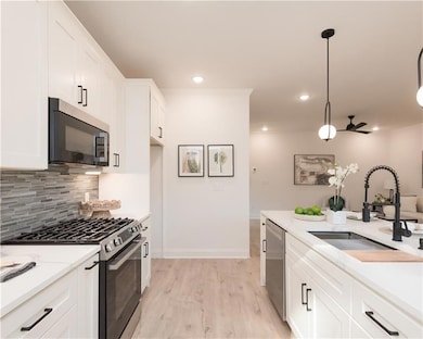 Kitchen featuring stainless steel appliances, white cabinetry, decorative light fixtures, light stone countertops, and decorative backsplash