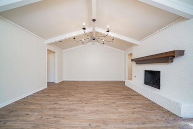Unfurnished living room with wood finished floors, a chandelier, and a brick fireplace