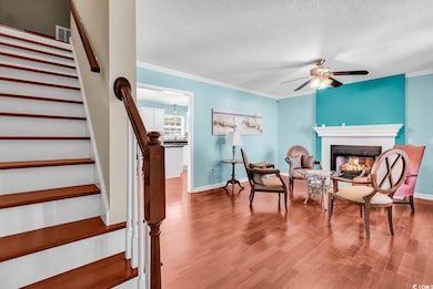 Living area with stairway, crown molding, a textured ceiling, ceiling fan, and wood finished floors
