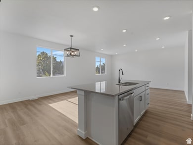 Kitchen with pendant lighting, dishwasher, an island with sink, light wood finished floors, and white cabinets
