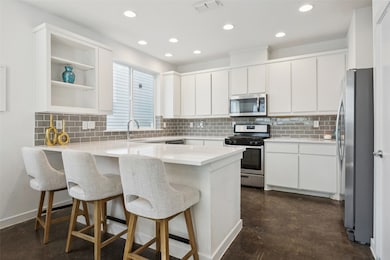 Kitchen with white cabinets, tasteful backsplash, stainless steel appliances, a peninsula, and a kitchen breakfast bar