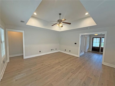 Empty room with a tray ceiling, a ceiling fan, light wood-type flooring, and recessed lighting