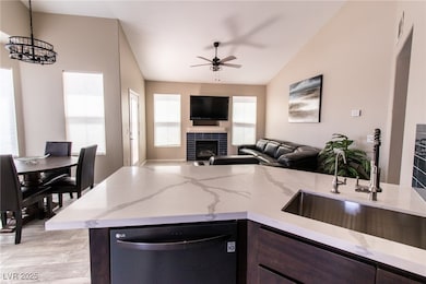 Kitchen with dishwasher, dark brown cabinets, a fireplace, light stone countertops, and decorative light fixtures
